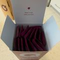 An open box containing multiple dark purple or burgundy colored packets arranged in rows, with text on the inside lid that reads "Sleep in rest, wake your best."