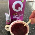 A white mug containing a dark red beverage with a spoon, next to a purple PurQ Night Time Restore supplement box on a kitchen counter