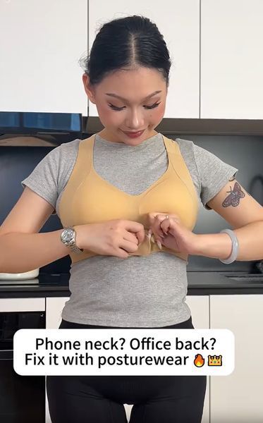 Woman in kitchen wearing yellow posture-correcting garment over gray shirt, demonstrating proper posture alignment