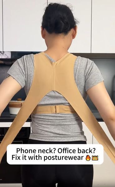 Person wearing a beige posture correction device over a gray shirt in a kitchen setting
