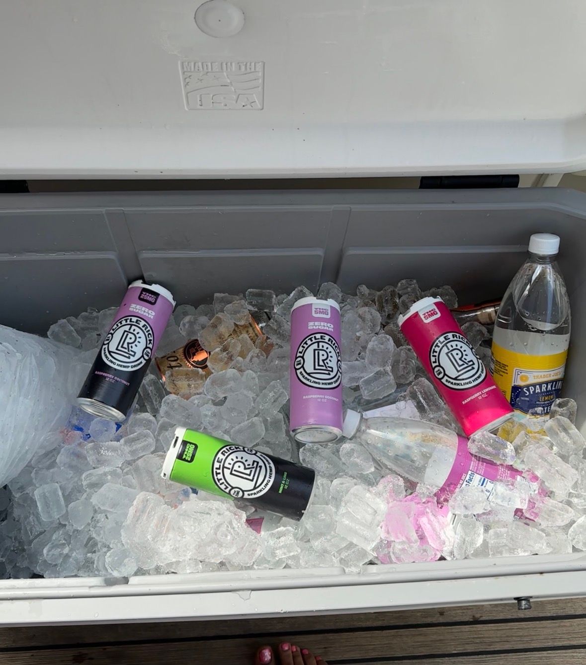 A cooler filled with ice containing several colorful beverage cans and a water bottle