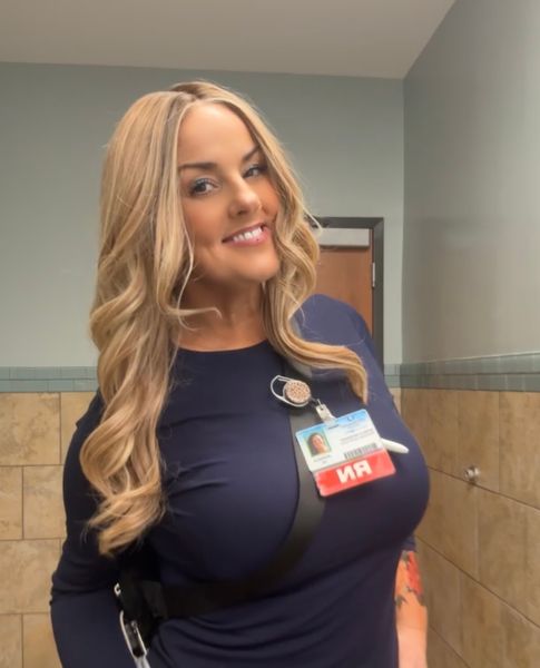 Customer-uploaded image. The image represents: A woman with long blonde hair wearing a dark blue top and an ID badge, smiling in what appears to be an office or workplace setting