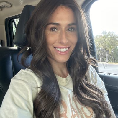 Customer-uploaded image. Click to see more details. The image represents: Woman with long brown hair smiling while sitting in a car wearing a light colored sweatshirt