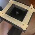 A wooden frame with masking tape attached to what appears to be a dark electronic device or screen, held by hands