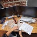 Person assembling furniture at wooden desk with dual monitors, instruction manual, and various hardware components spread out