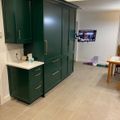 Modern kitchen with dark green cabinets, white countertops, brass hardware, and beige tile flooring in an open living space