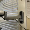 A security camera mounted on a wall bracket next to white horizontal blinds covering a window
