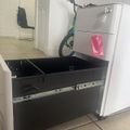 A unicycle stored in a pull-out drawer beneath a refrigerator in a kitchen