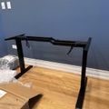 Black adjustable desk frame being assembled on wooden floor in room with blue walls