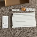 Cable management kit components laid out on carpet including white plastic channels, mounting brackets, instruction manual, and cardboard packaging box