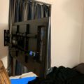 A flat screen TV mounted on an adjustable wall bracket in a bedroom with striped curtains and bedding visible