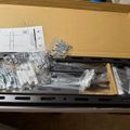 An unboxed product with assembly instructions, metal hardware pieces in plastic bags labeled W-A, W-B, W-C, and a black metal frame or bracket laid out in cardboard packaging