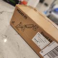 A cardboard box labeled "MOUNT-IT!" with "Dual Monitor" text and a diagram showing a dual monitor mount, sitting on a white surface