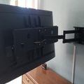 A large flat-screen TV mounted on an articulating wall bracket that extends from the wall, positioned above a wooden dresser in a living room setting