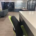 Modern office interior with green and black chairs at white desk, tiled flooring, and glass-walled meeting rooms in background