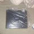 A black electronic device or mount labeled "MOUNT-IT" wrapped in clear plastic packaging, sitting on a white surface next to a white basket