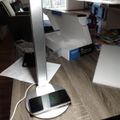 A white LED desk lamp with a circular base that doubles as a wireless charging pad, with a smartphone placed on it for charging