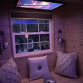 Cozy wooden interior with window seat, knitted pillows, and colorful ceiling light displaying sunset sky