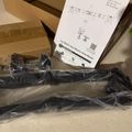 Unboxed dual monitor desk mount with instruction manual and mounting hardware in plastic packaging