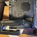 Overhead view of a computer monitor stand and base assembly with mounting hardware, cables, and connection ports visible on a wooden desk surface.