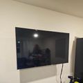 Wall-mounted flat screen TV with black screen showing reflections, with a power drill visible on a surface below