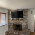 Living room with brick fireplace, mounted TV above wooden mantel, and window with wooden blinds