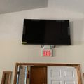 Wall-mounted TV above an exit sign and doorway in an indoor room