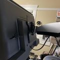 A computer monitor mounted on an adjustable arm above a desk with various office supplies and equipment visible below