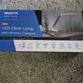 Package box for MOUNT-IT! LED Desk Lamp with Wireless Charging featuring product image and specifications on gray carpet