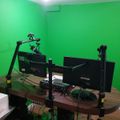A home office setup with multiple monitors on adjustable arms positioned on a wooden desk, with bright green walls creating a vibrant workspace environment