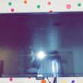 A flat-screen TV mounted on a white wall decorated with colorful polka dot stickers, with the screen reflecting light from the room