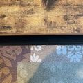 A decorative fabric or tapestry with floral patterns displayed on a wooden surface with black mounting hardware