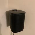 Black Sonos speaker mounted on white wall with power cord visible