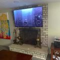 Living room with brick fireplace, mounted flat screen TV displaying city skyline, colorful artwork on wall, and wooden furniture