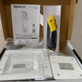 Open cardboard box containing a Mount-It in-wall TV cable concealer kit with white mounting plates, installation manual, and yellow-handled tool