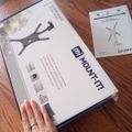 A hand placed next to a TV mount product box and instruction manual on a wooden floor