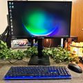 Computer workstation with monitor displaying colorful desktop wallpaper, blue backlit keyboard, mouse, and decorative plants on wooden desk