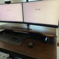 Dual monitor computer workstation with two screens displaying Google homepage, keyboard and mouse on wooden desk