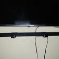 A Hisense TV mounted on a white wall with a black soundbar positioned below it, connected by visible cables