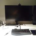 A computer workstation with a large monitor, keyboard, mouse, small desk fan, and various cables on a white desk