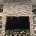 Living room entertainment center with mounted flat screen TV on stone accent wall, flanked by white built-in shelving units displaying decorative items and topped with green plants