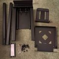 Disassembled dark wooden furniture parts and hardware pieces laid out on beige carpet, including rails, panels, brackets and screws for assembly