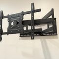 Full motion TV wall mount bracket with articulating arms, mounted on a white wall, featuring adjustable VESA compatibility and cable management slots.