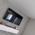 A flat-screen TV mounted on a ceiling above a white shelf with decorative items and baskets.
