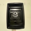 Wall-mounted black security device or intercom system with metallic components visible inside the open housing