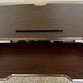 A wooden standing desk converter with two tiers - an upper surface for a monitor or laptop and a lower keyboard tray, both with curved ergonomic cutouts