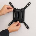 Two hands holding a black MOUNTIT TV wall mount bracket with four articulating arms against a white background.