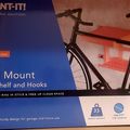 Product packaging for a Mount-It bike wall mount with shelf and hooks, showing a bicycle mounted on a wall storage system