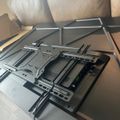 TV wall mount bracket with articulating arms lying on a glass table next to packaging materials