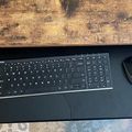 A black keyboard tray or desk surface with a wireless keyboard and mouse, mounted under a wooden desk